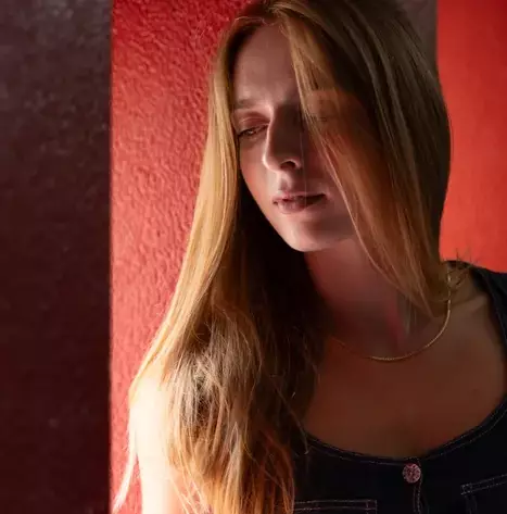 Photographie d'une jeune femme en lumière naturelle dans un environnement existant (une cage d'escalier des fenêtres et un mur entièrement rouge)