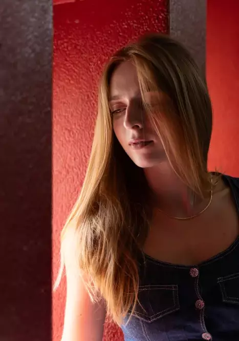 Photographie d'une jeune femme en lumière naturelle dans un environnement existant (une cage d'escalier des fenêtres et un mur entièrement rouge)