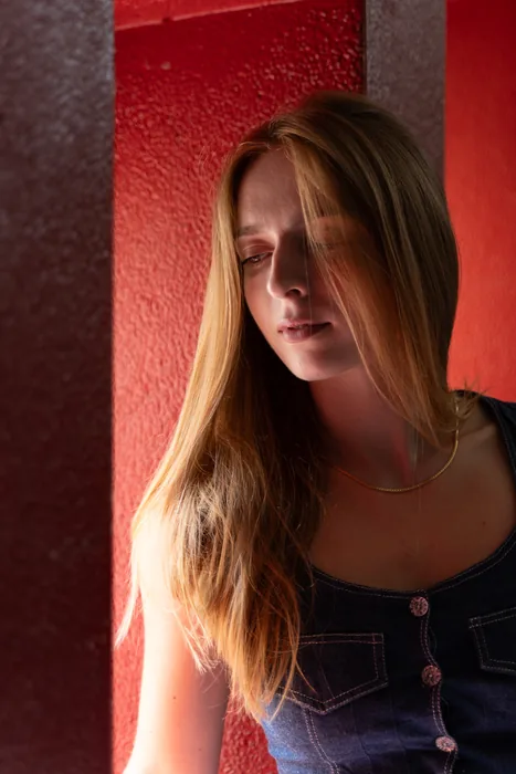 Photographie d'une jeune femme en lumière naturelle dans un environnement existant (une cage d'escalier des fenêtres et un mur entièrement rouge)